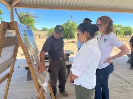 Secretary Haaland and two others in BLM shirts view a map outdoors.