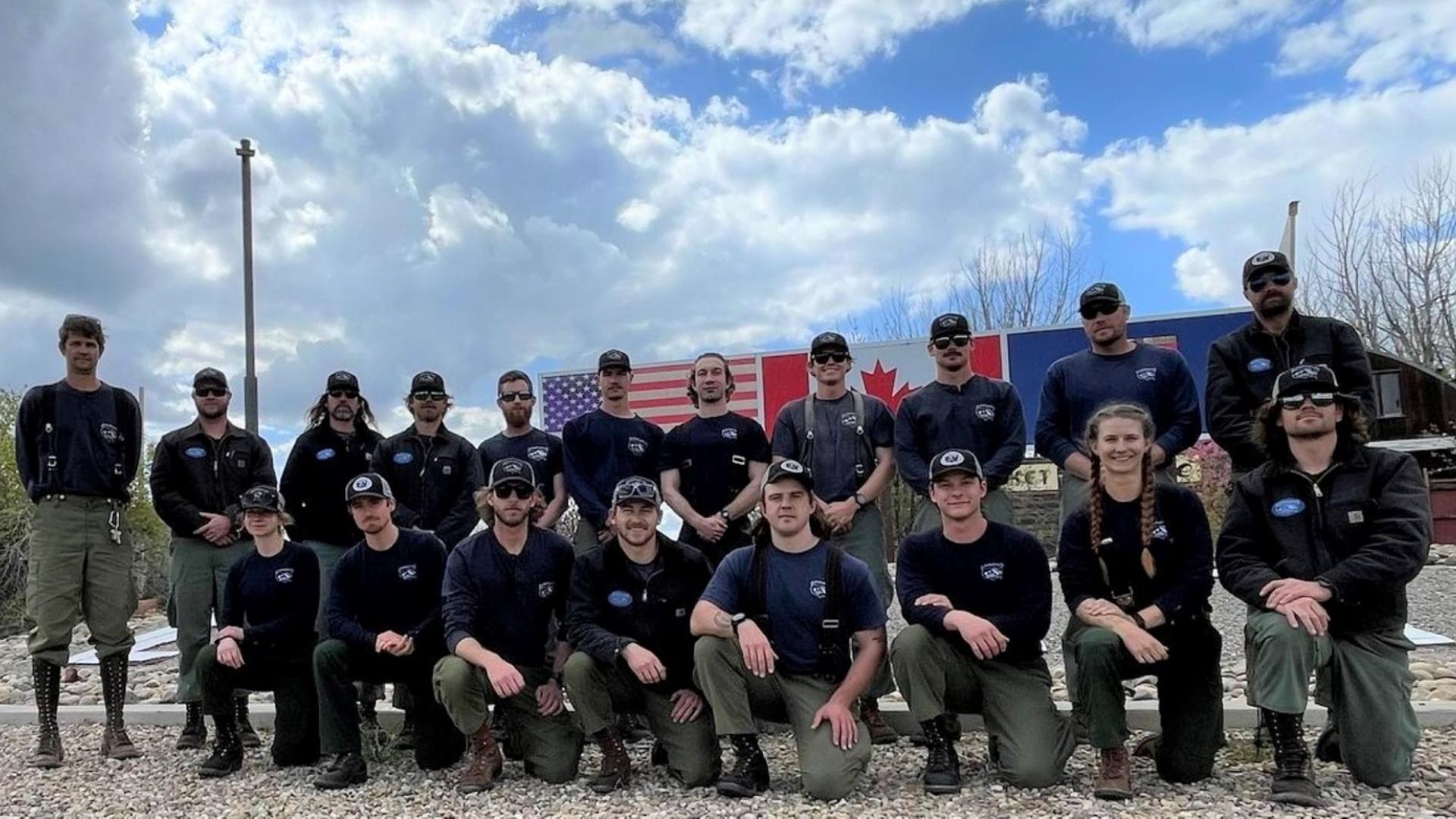 A National Park Service hotshot crew stands in a group before US and Canada flags.