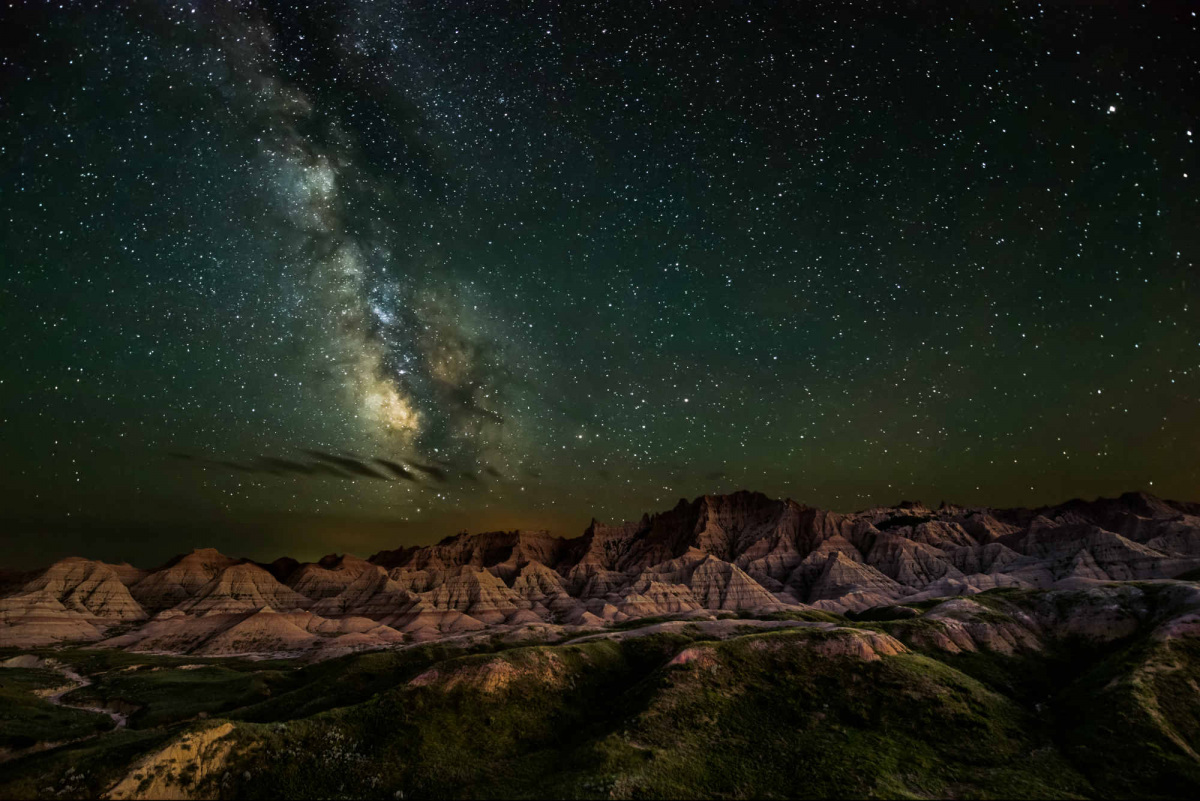 The Milky Way appears in a green starry sky, illuminating the mountain-filled landscape below.