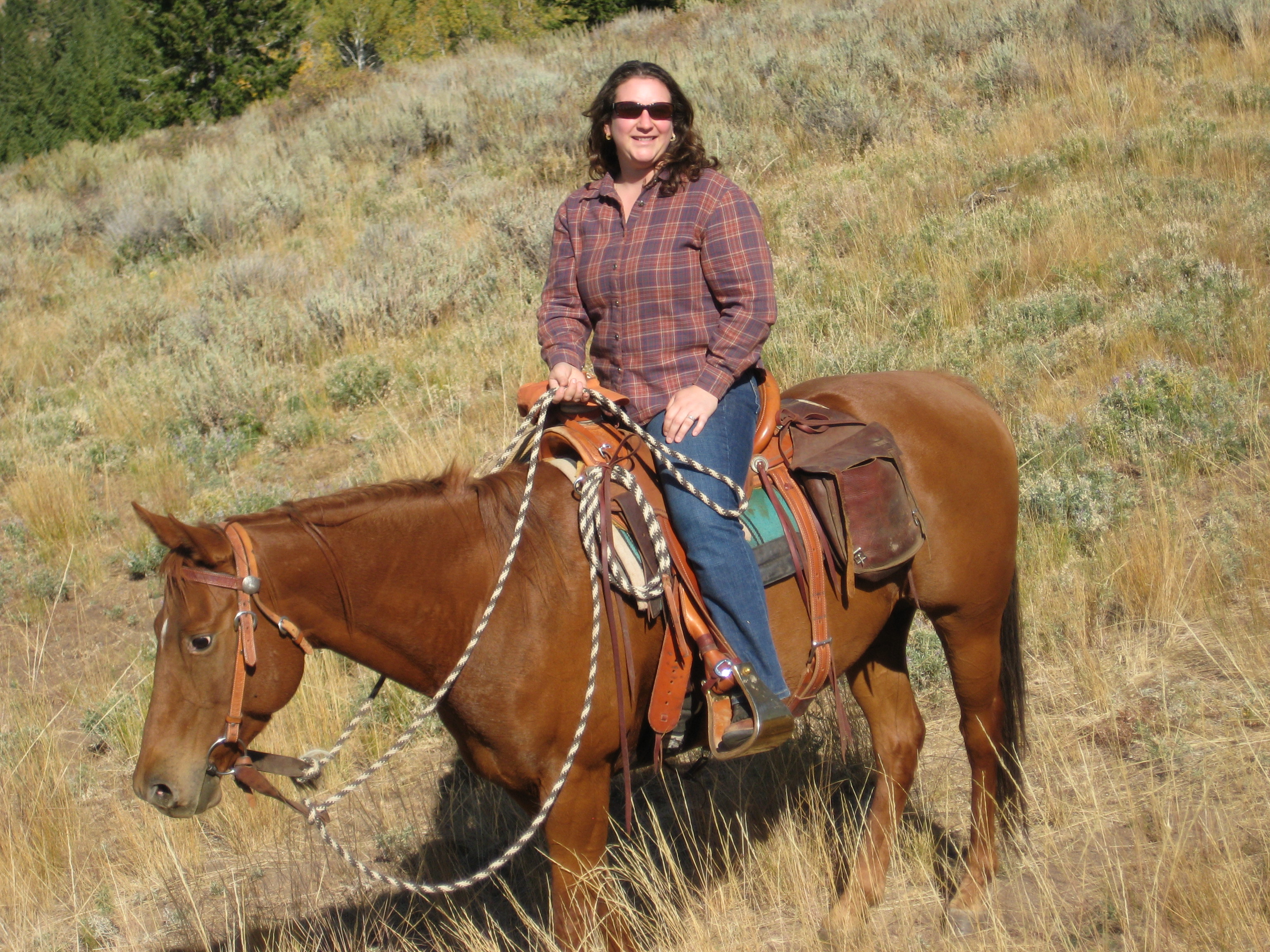Joanna sitting on a horse in a western saddle surrounded by grasslands.