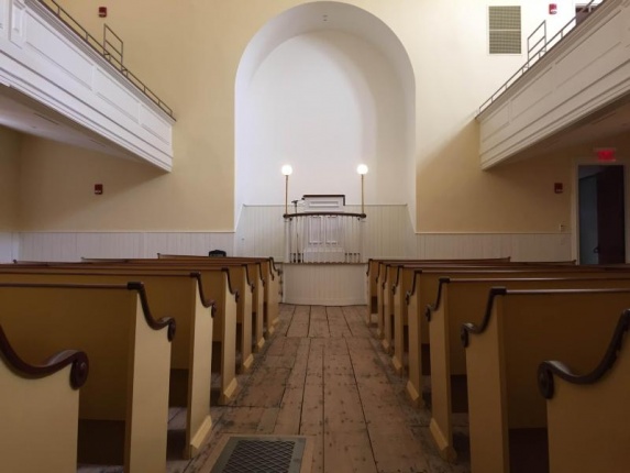 The inside of the African Meeting House has a long aisle lined with wooden pews.