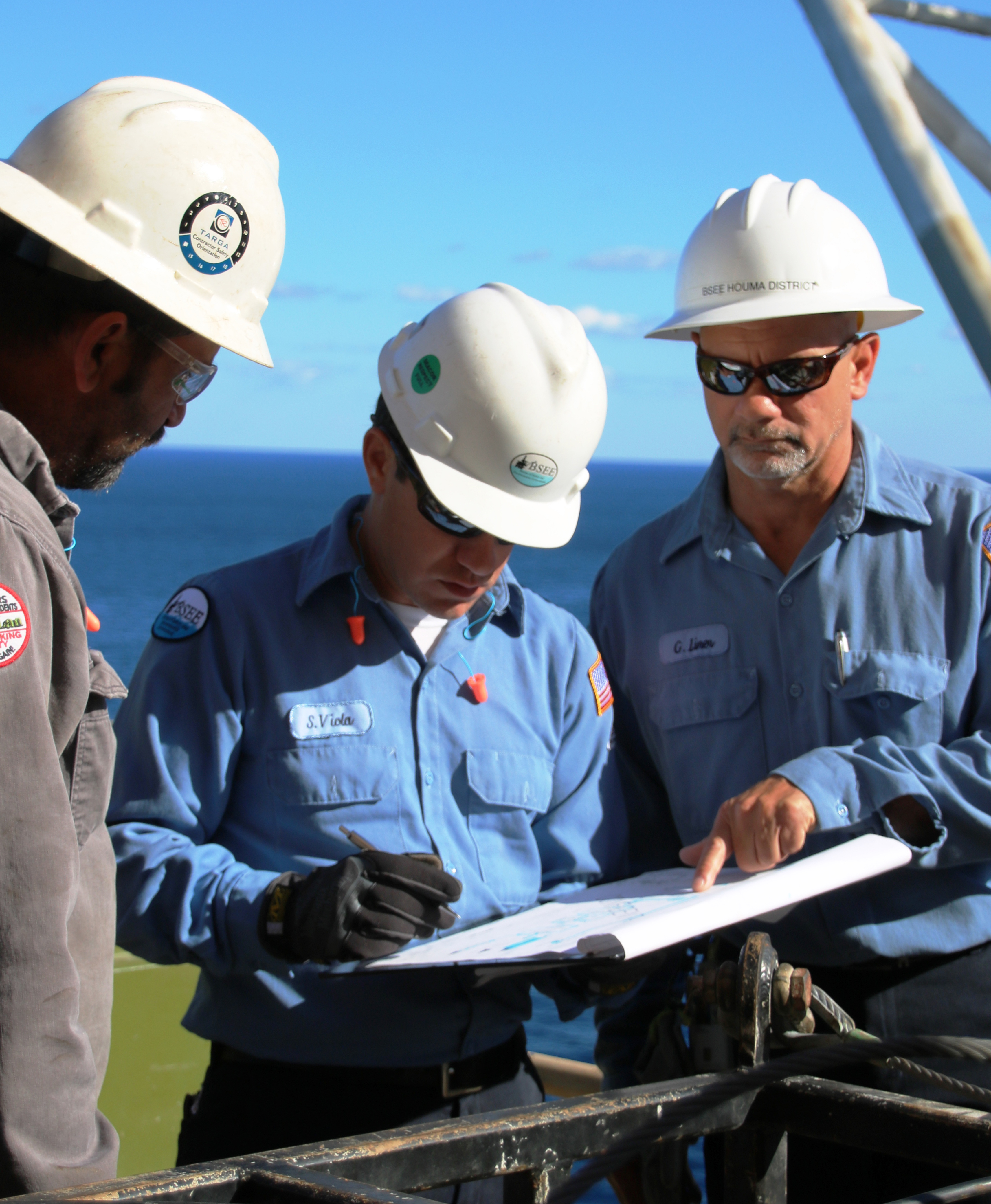 Three male engineers review a work plan with water in the background.