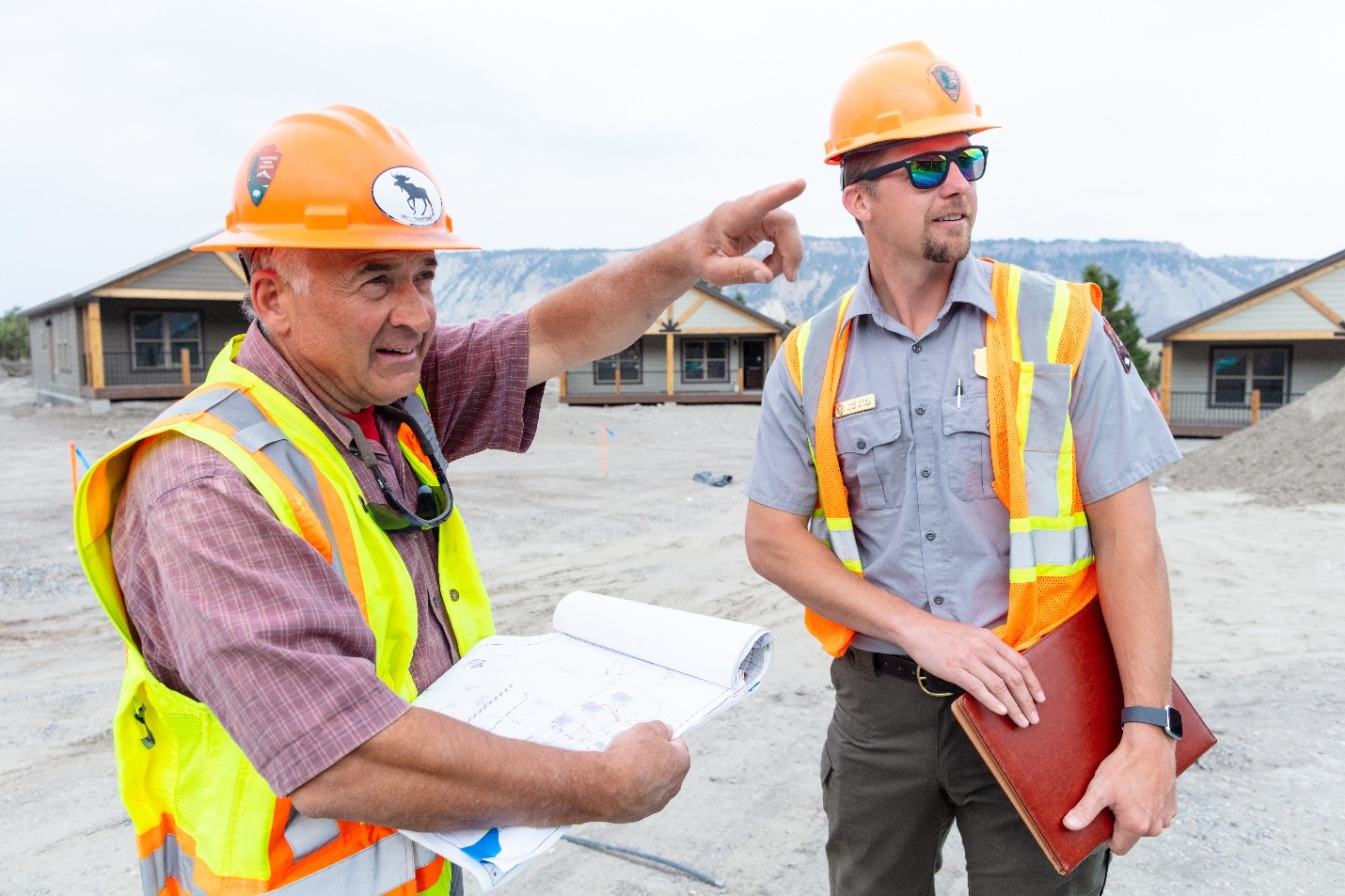 Two engineers with hard hats observe a building site.