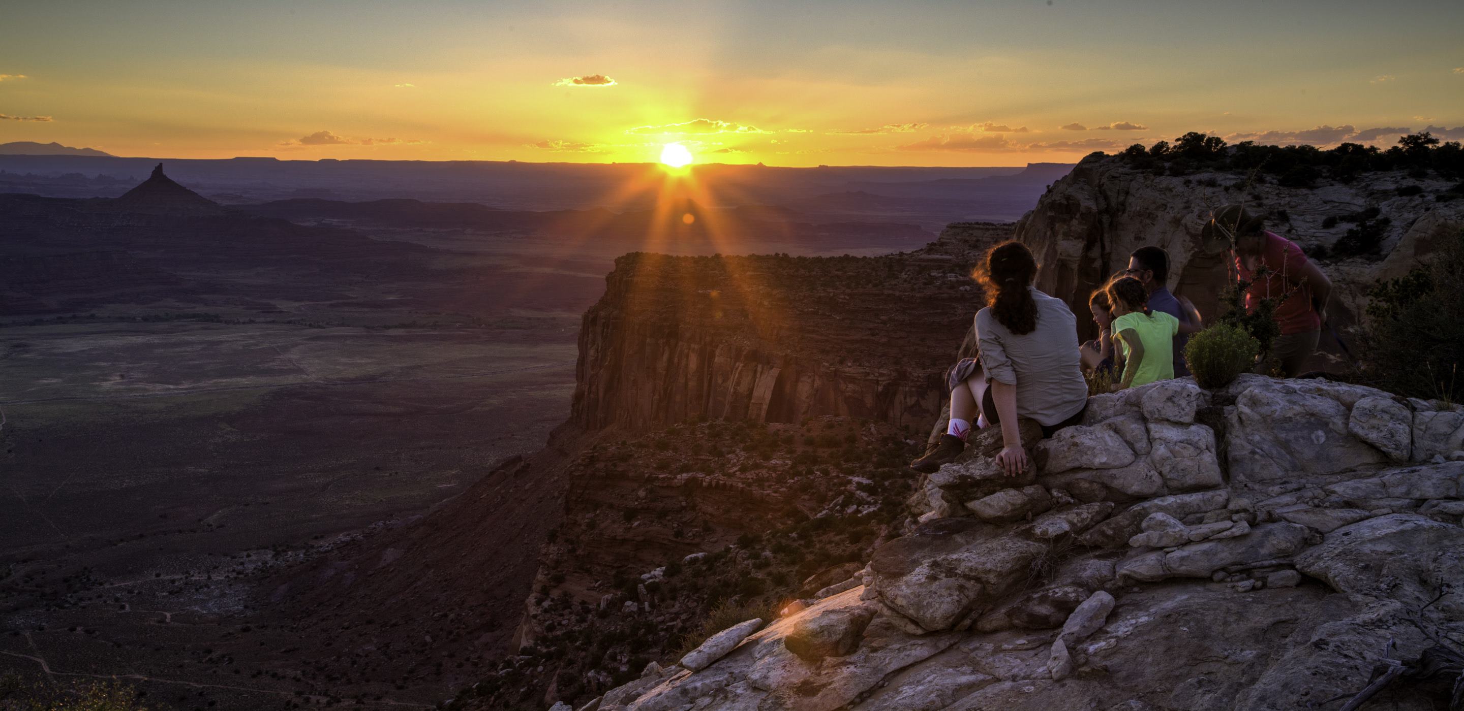 Hikers enjoy the sunset from a cliff overlooking a valley