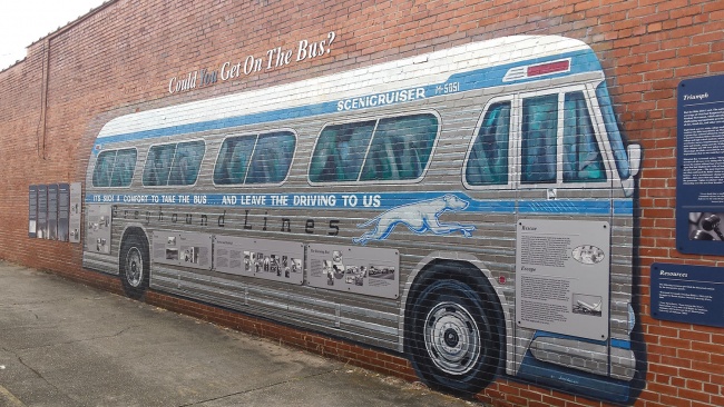 Historic mural of a large Greyhound bus painted on a long brick wall.