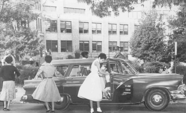 A historic black and white photo of two African American teenage girls getting out of a car in front of a large brick building.