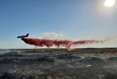 A small plane dumping red fire stopper onto scorched and smoky earth