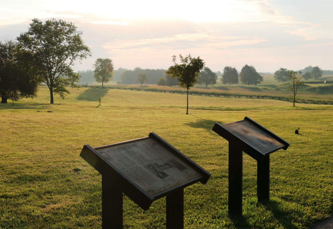 Two informational plaques stand on a grassy field near a wooden fence.