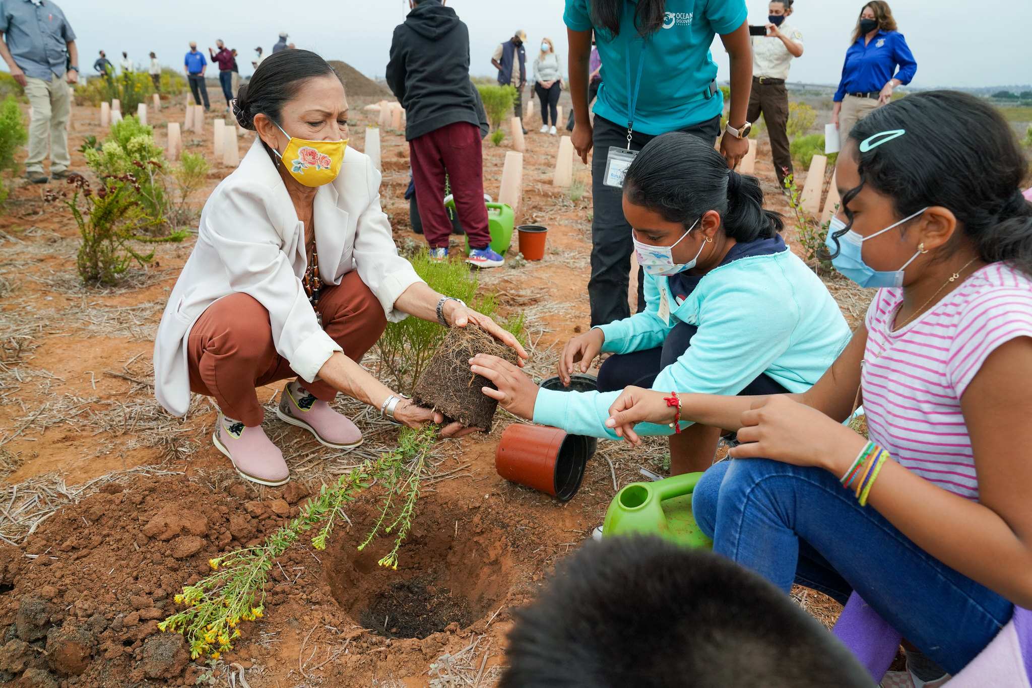 Secretary Haaland plants a tree alongside children at the San Diego Wildlife Refuge.
