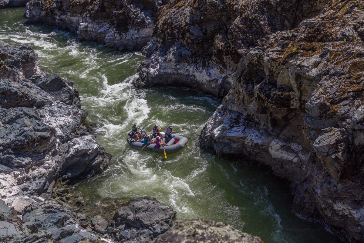 A family rafts down the Rogue River, encompassed by large rock walls.