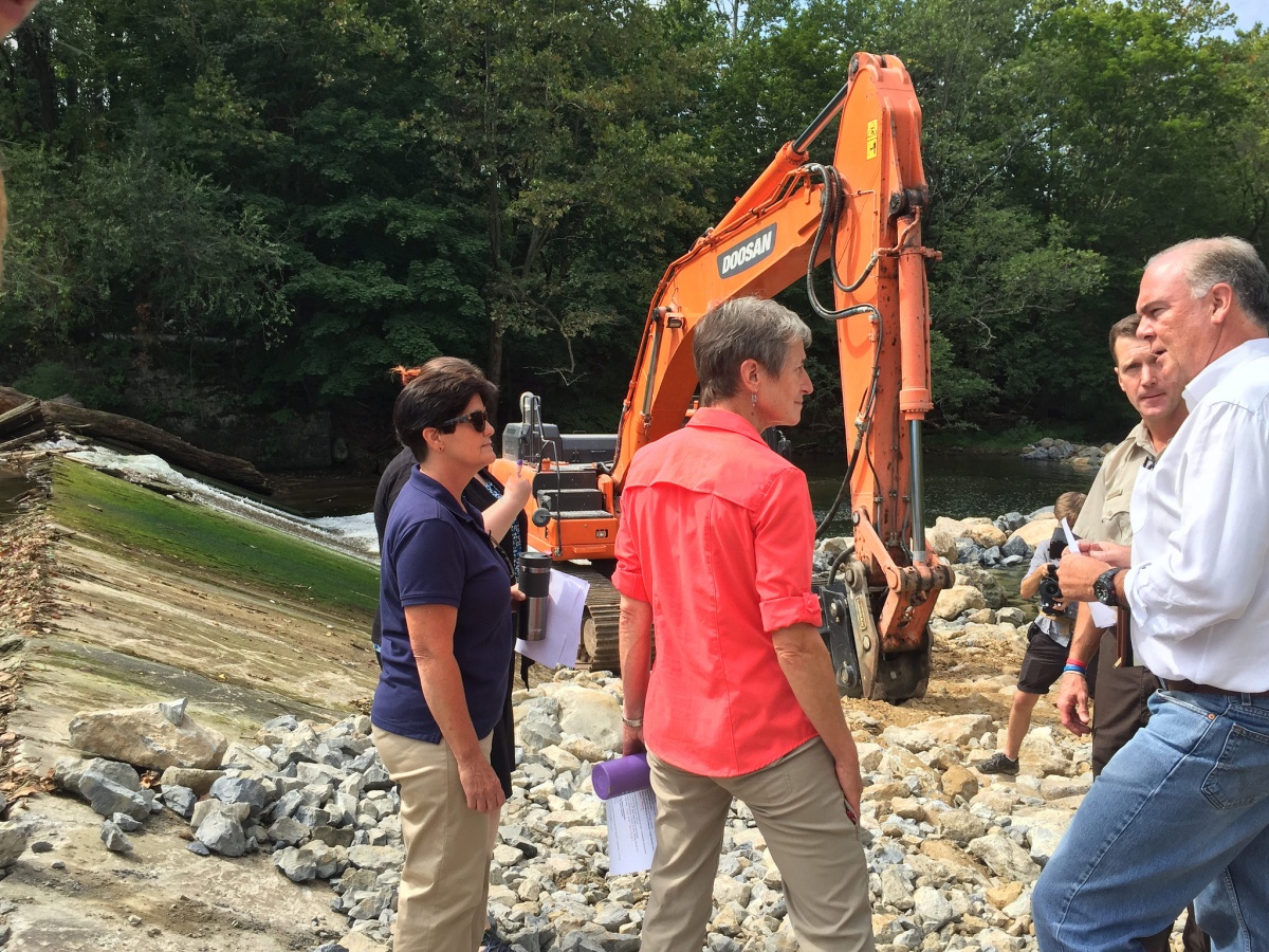 Secretary Jewell standing with a group of people next to construction equipment along the Musconetcong River.