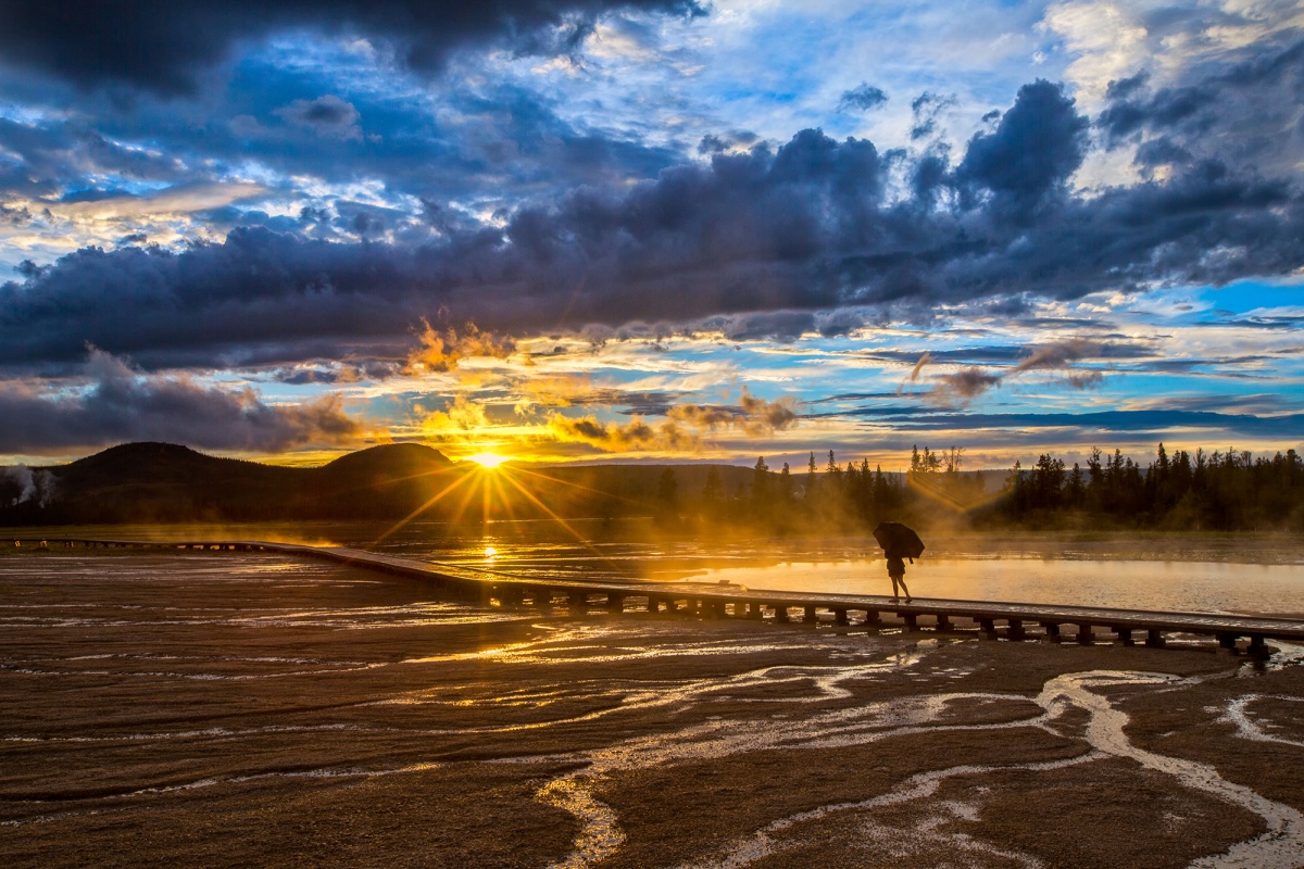 A lone visitor walks along the thermal ponds as the sun rises over the mountains. 