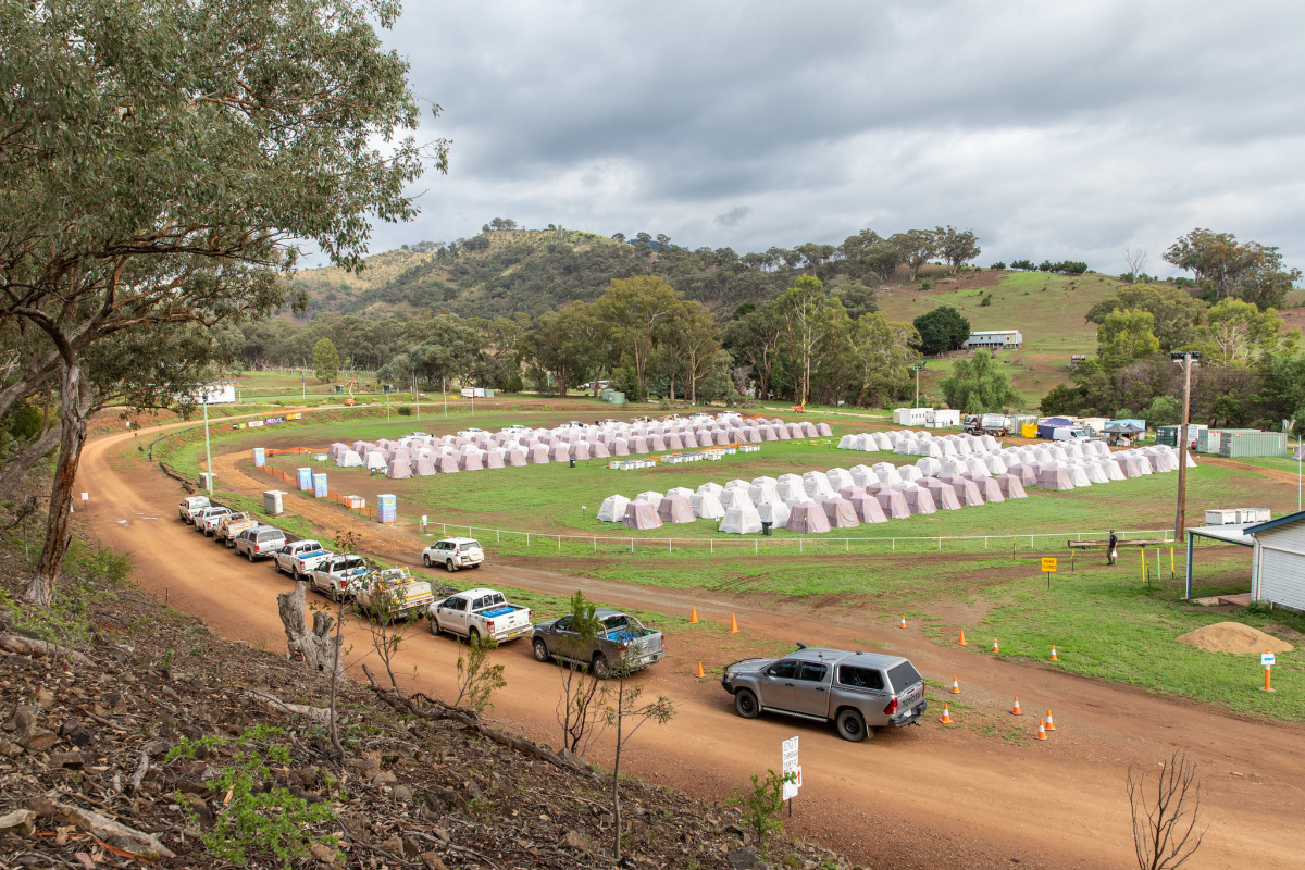 A row of trucks parked next to a field with rows of tents