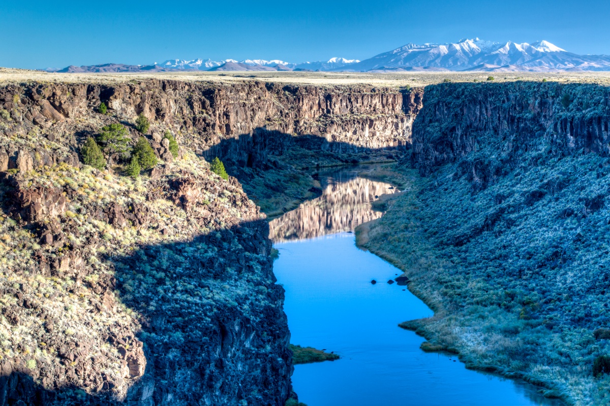 A shadow from the canyon walls falls over the still turquoise blue Rio Grande. 