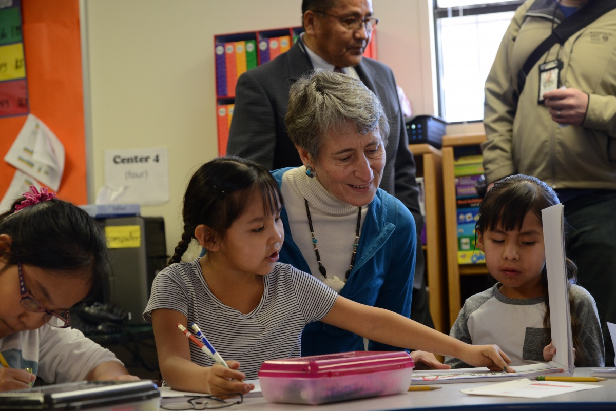 Secretary Jewell sits at a table with Native American students in a classroom.