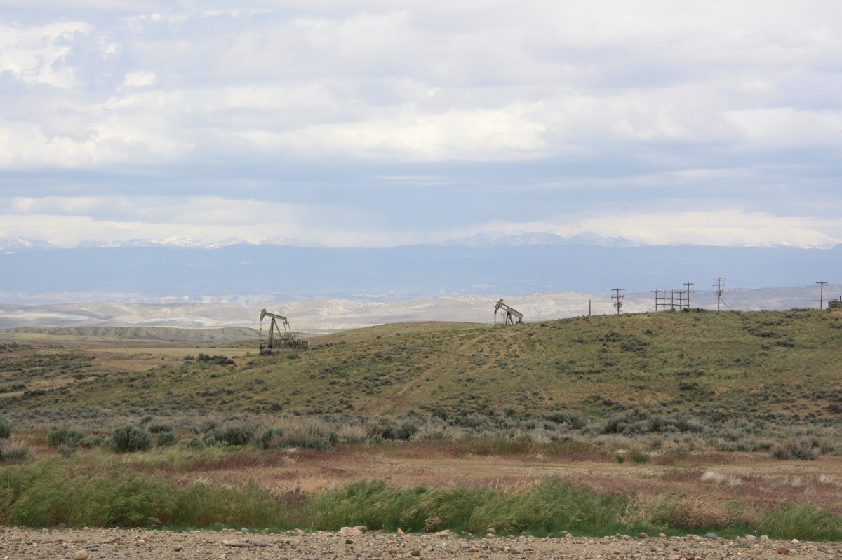 Two oil pumpers dot rolling hills with mountains looming in the distance.  