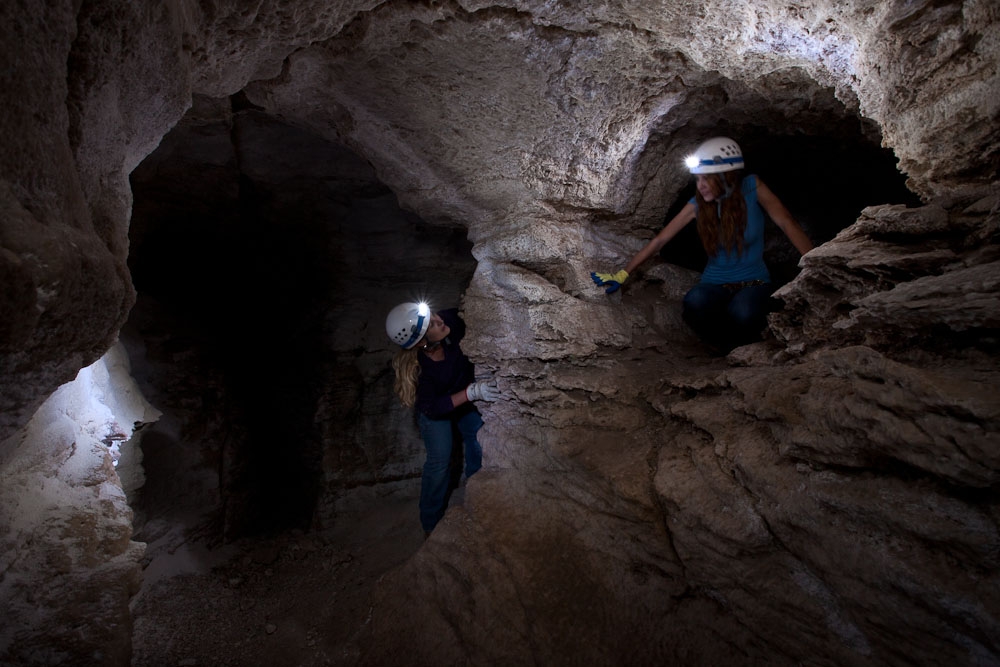 two ladies explore a cave with headlamps