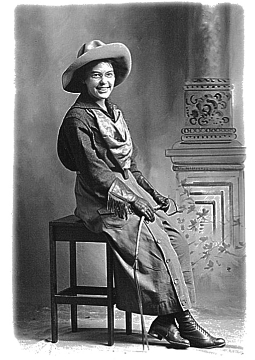 A historic back and white photo of a woman wearing a cowboy hat and a riding dress sitting on a small table.