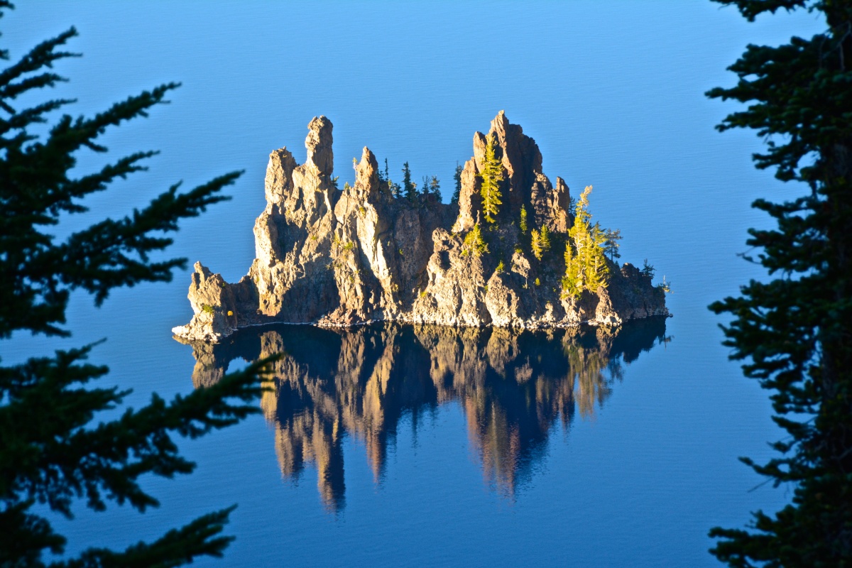A small island with tall rock towers and a few trees rises out of the still waters of a lake.
