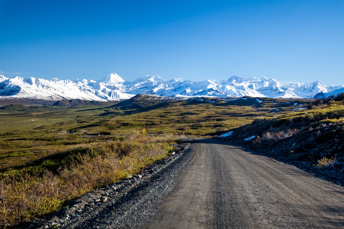 Long paved road spirals through vast green lands and mountains covered in snow
