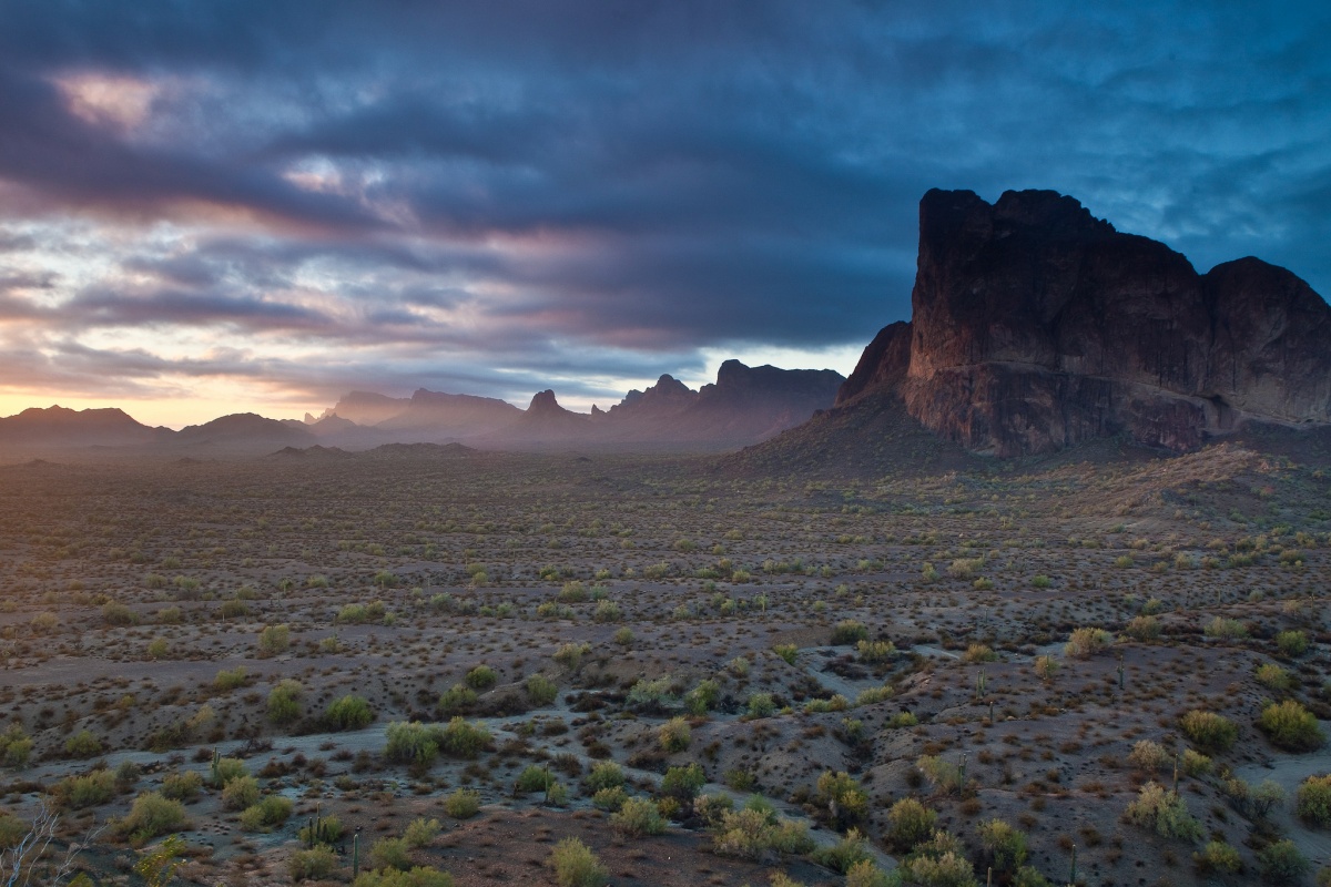 A dark stormy sky looms in the background as Eagle Tail Mountain juts up from a desert floor. 