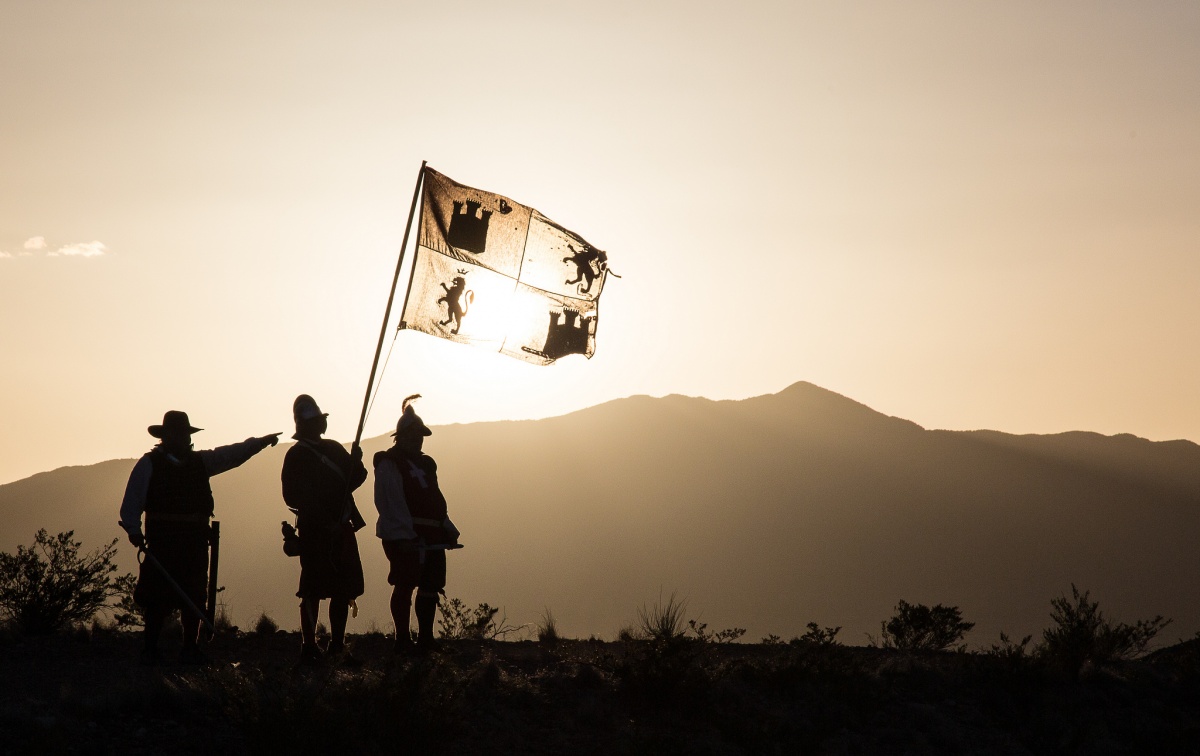3 people silhouetted point over a ridge with one person handling a flag 