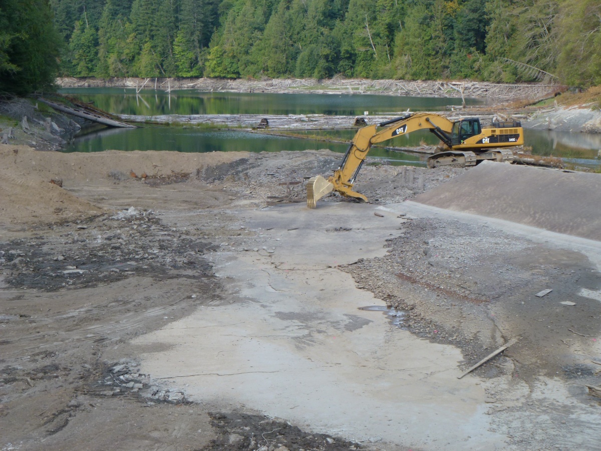 A large piece of heavy machinery moves dirt while removing a dam on a river.