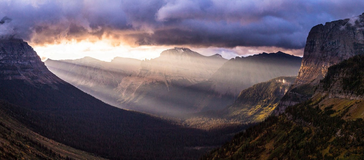 sun rays stream through clouds into a valley