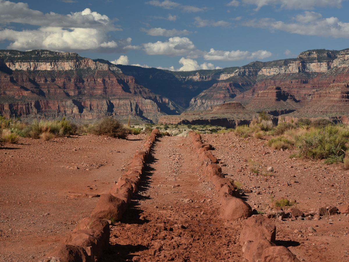 A rock lined trail leads straight towards a canyon with high rock walls.