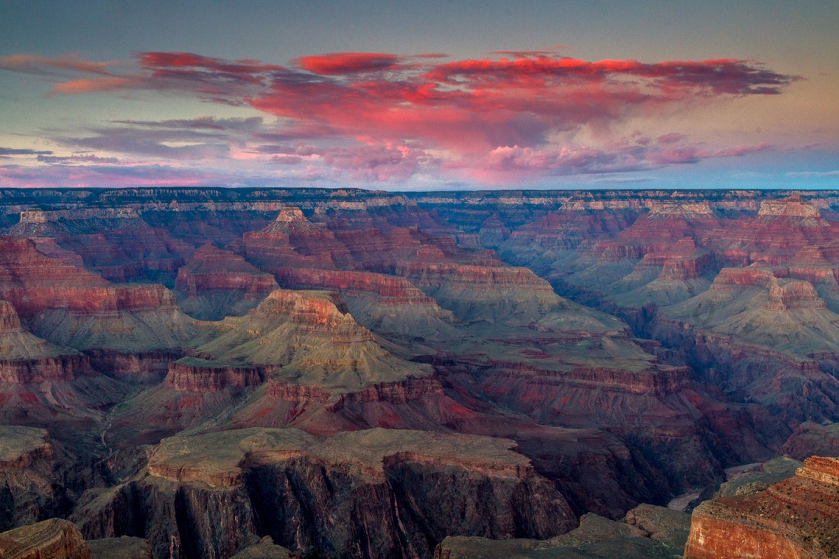 Pink sunset clouds float in the sky above a massive canyon landscape.