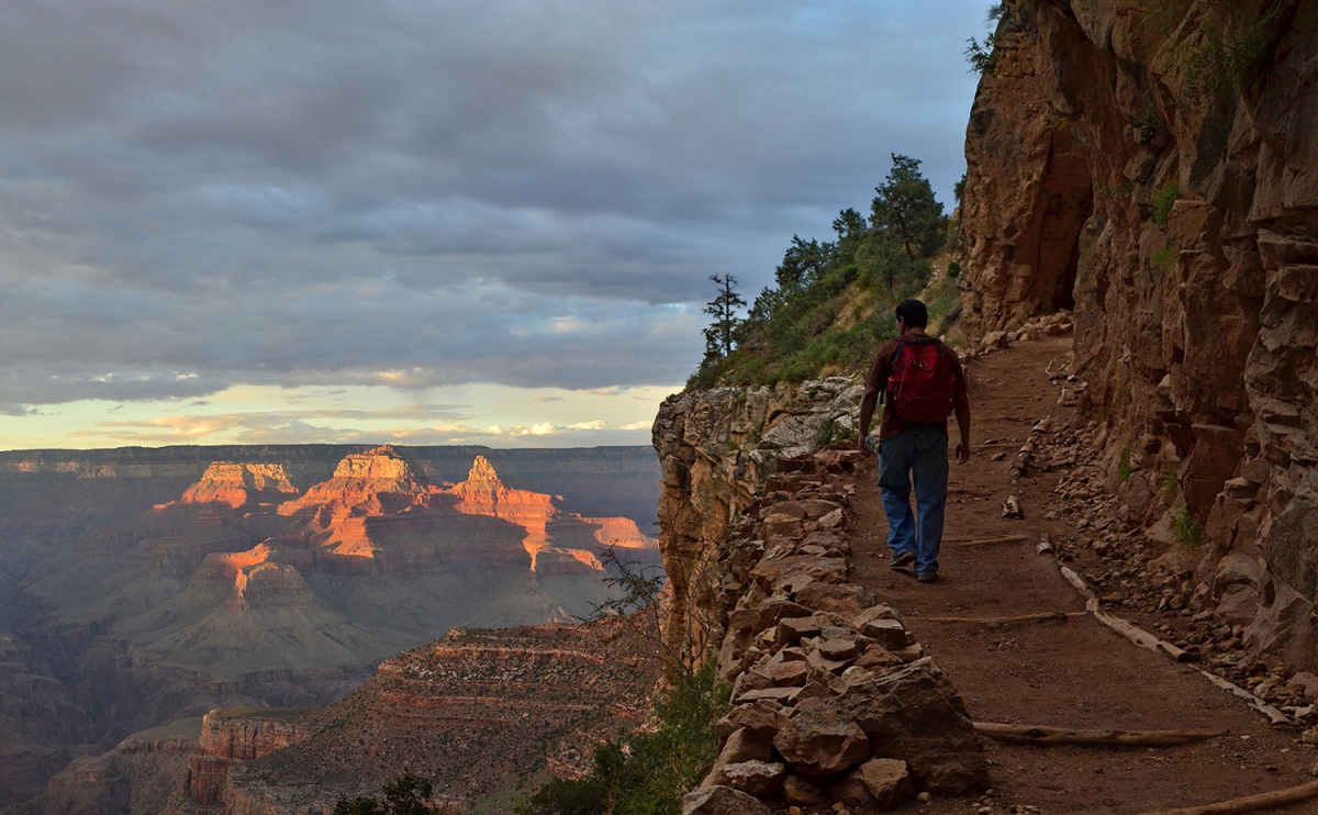 A hiker walks along a trail up the side of the Grand Canyon at sunset