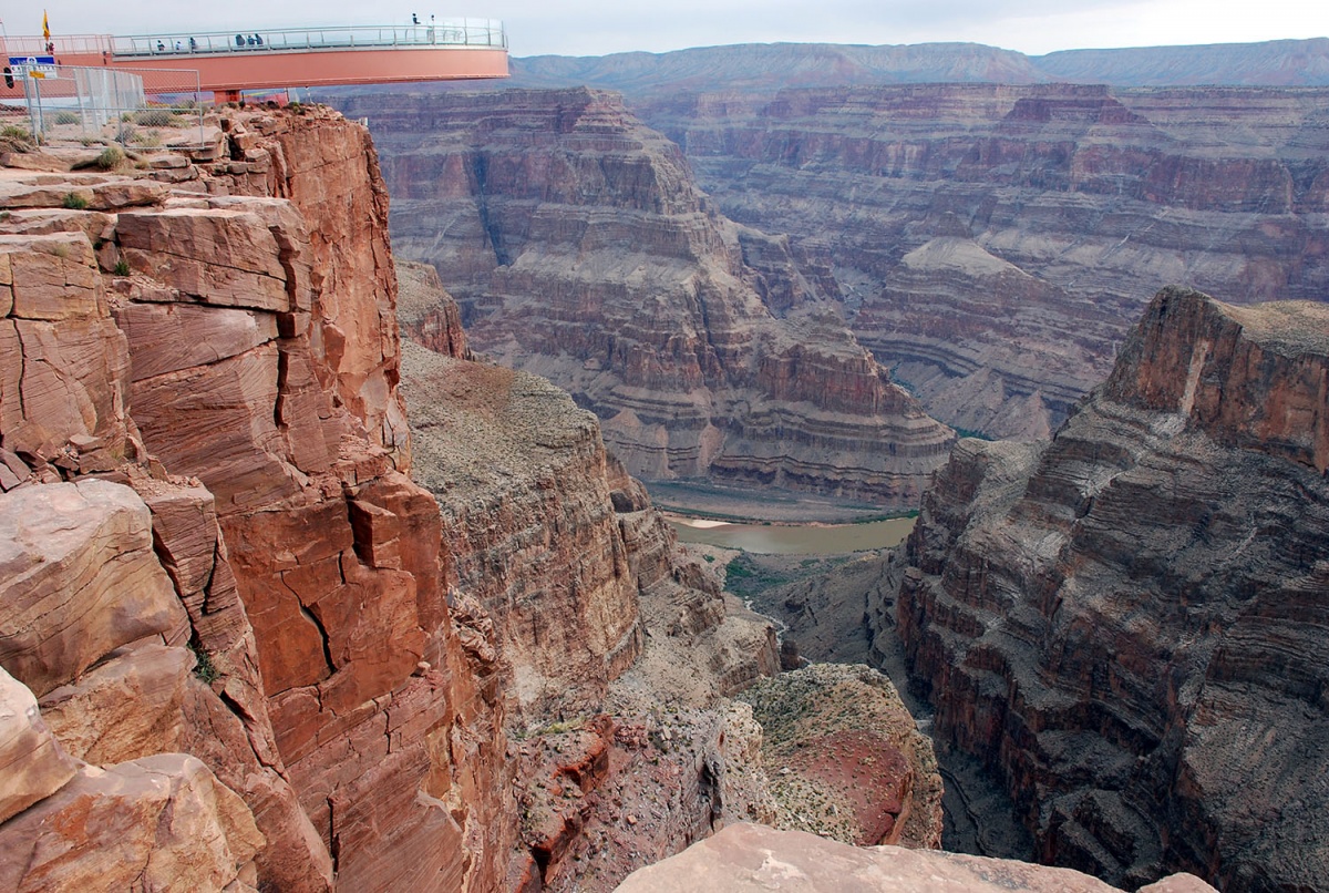 A pink walkway extends out over a purple and orange canyon, the Colorado river is seen below