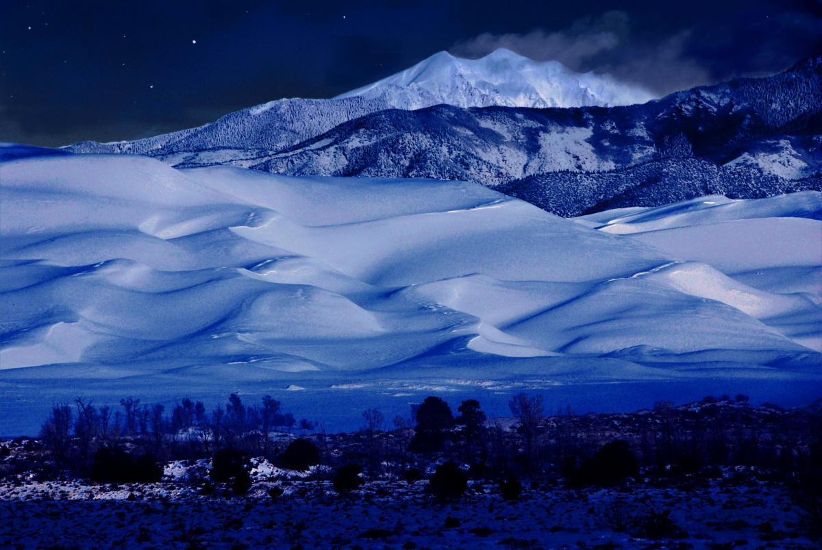 Frosty mist settles over a snow-capped mountain and snow-enveloped dunes. 