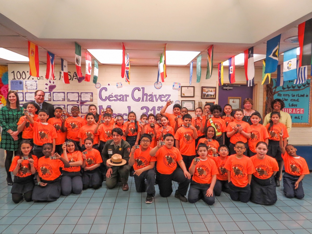 A group of students in orange shirts with teachers smiling in a classroom.