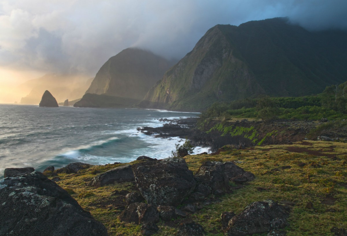 Mountains rise above an ocean shoreline at sunset.