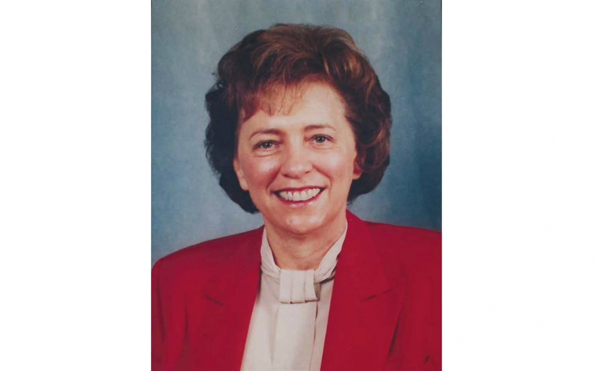 A head shot of a woman, Kathy Karpan, against a blue background. She is smiling and wearing a white blouse and a red blazer.