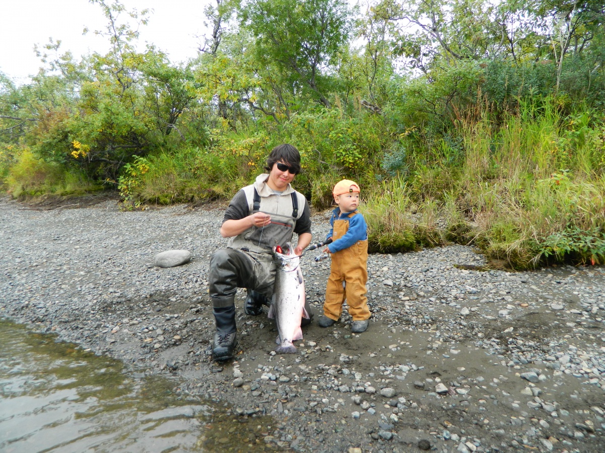 A teenager and a child hold a large fish on a river bank.