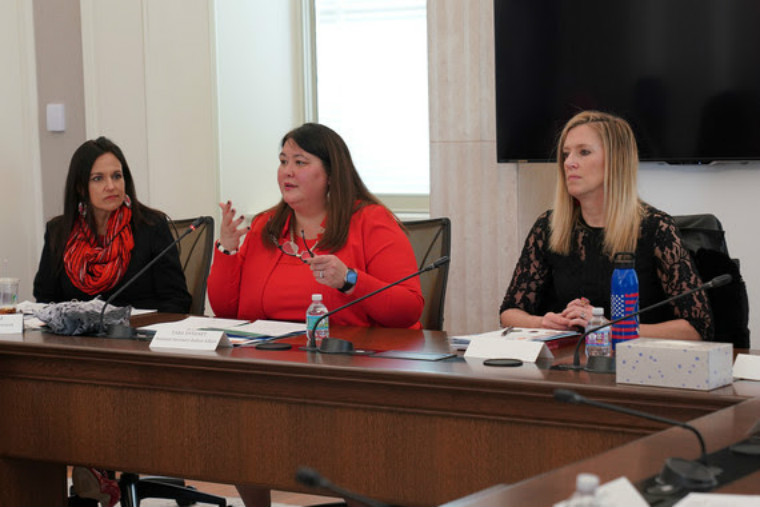 Three women in business suits sit at a table in a conference room.