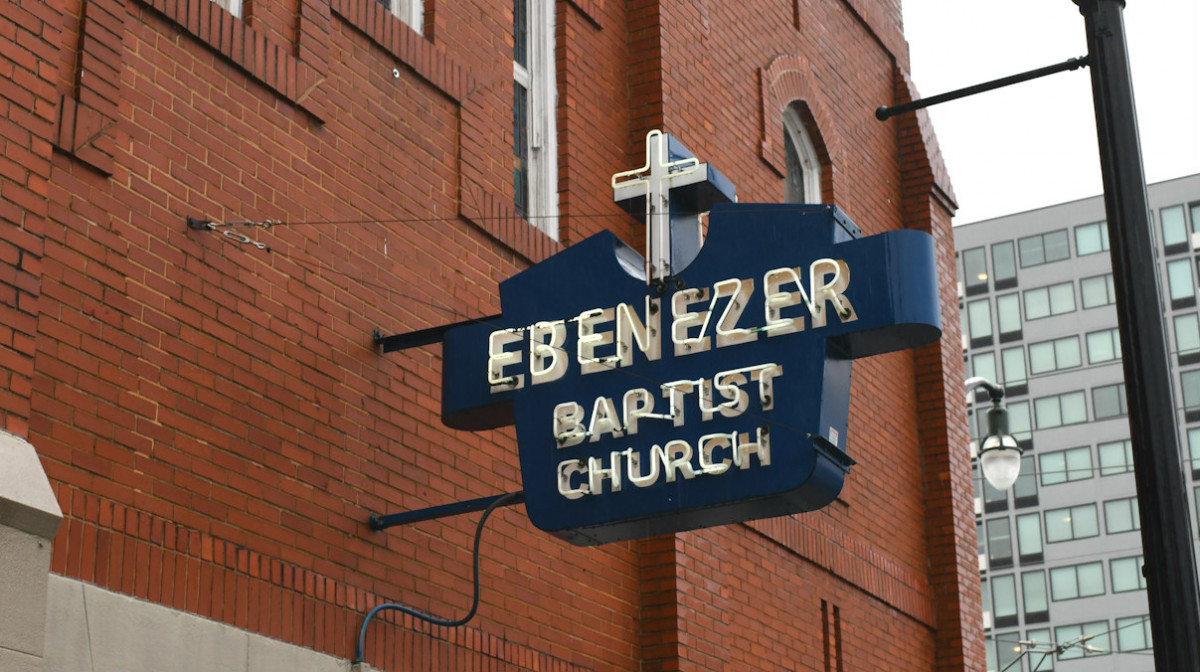 A metal sign reading Ebenezer Baptist Church hangs on the outside of a large brick building.