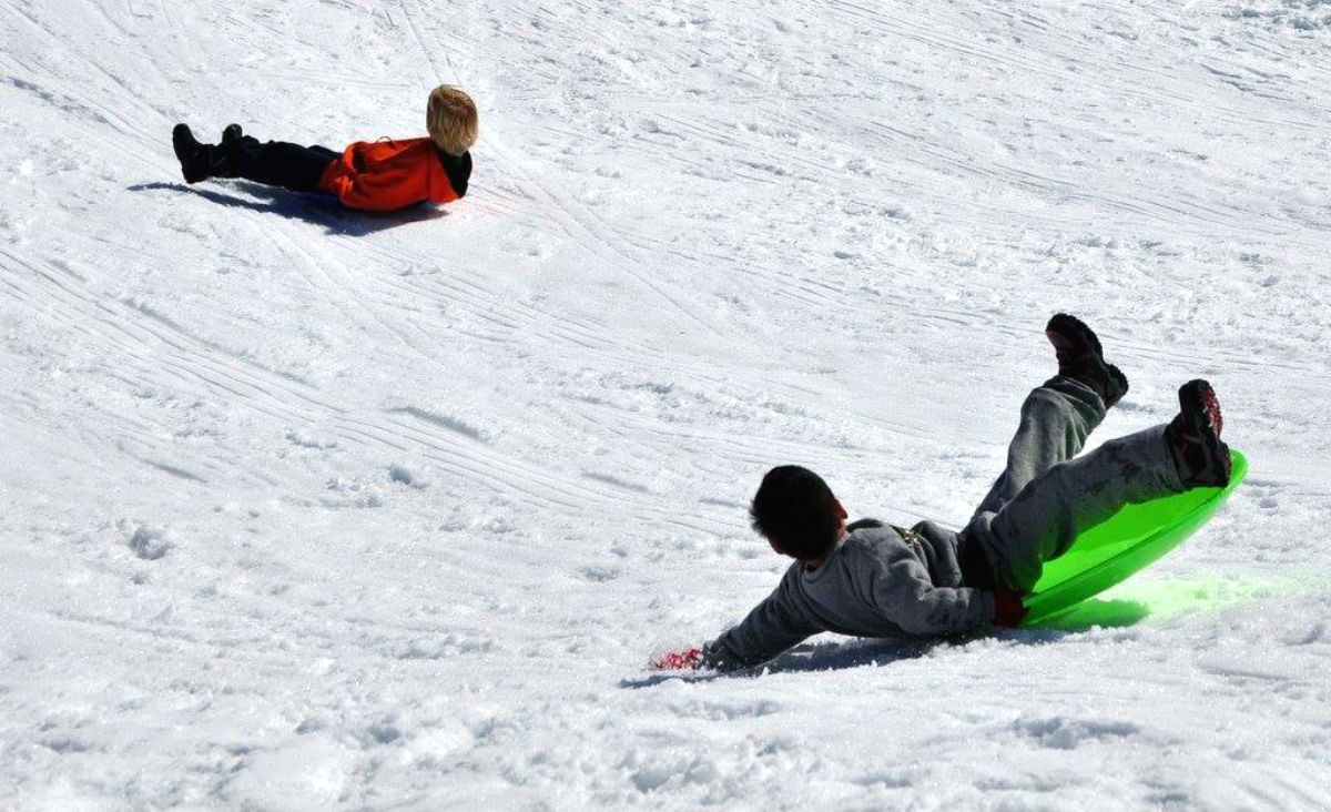 Two kids slide in dome shaped sleds on white, pristine snow.