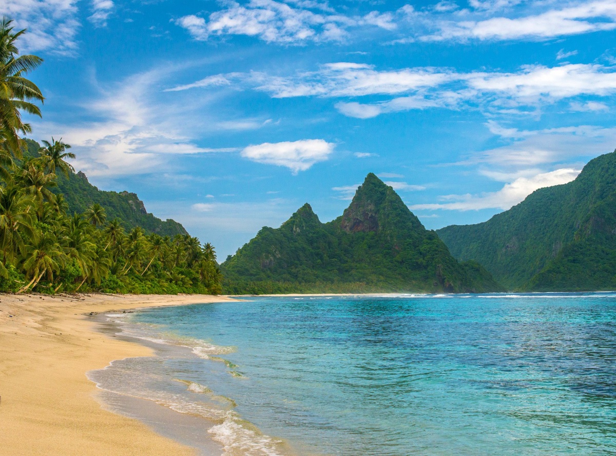 sandy beach, blue water, palm trees and green mountains