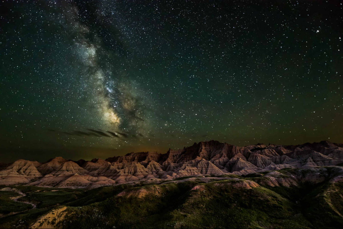 The milky way and a night sky full of stars hangs over a landscape of low rugged rock formations.