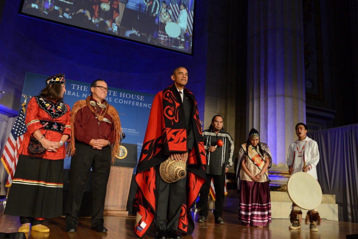 President Obama standing on a stage with native american leaders after receiving a ceremonial blanket.