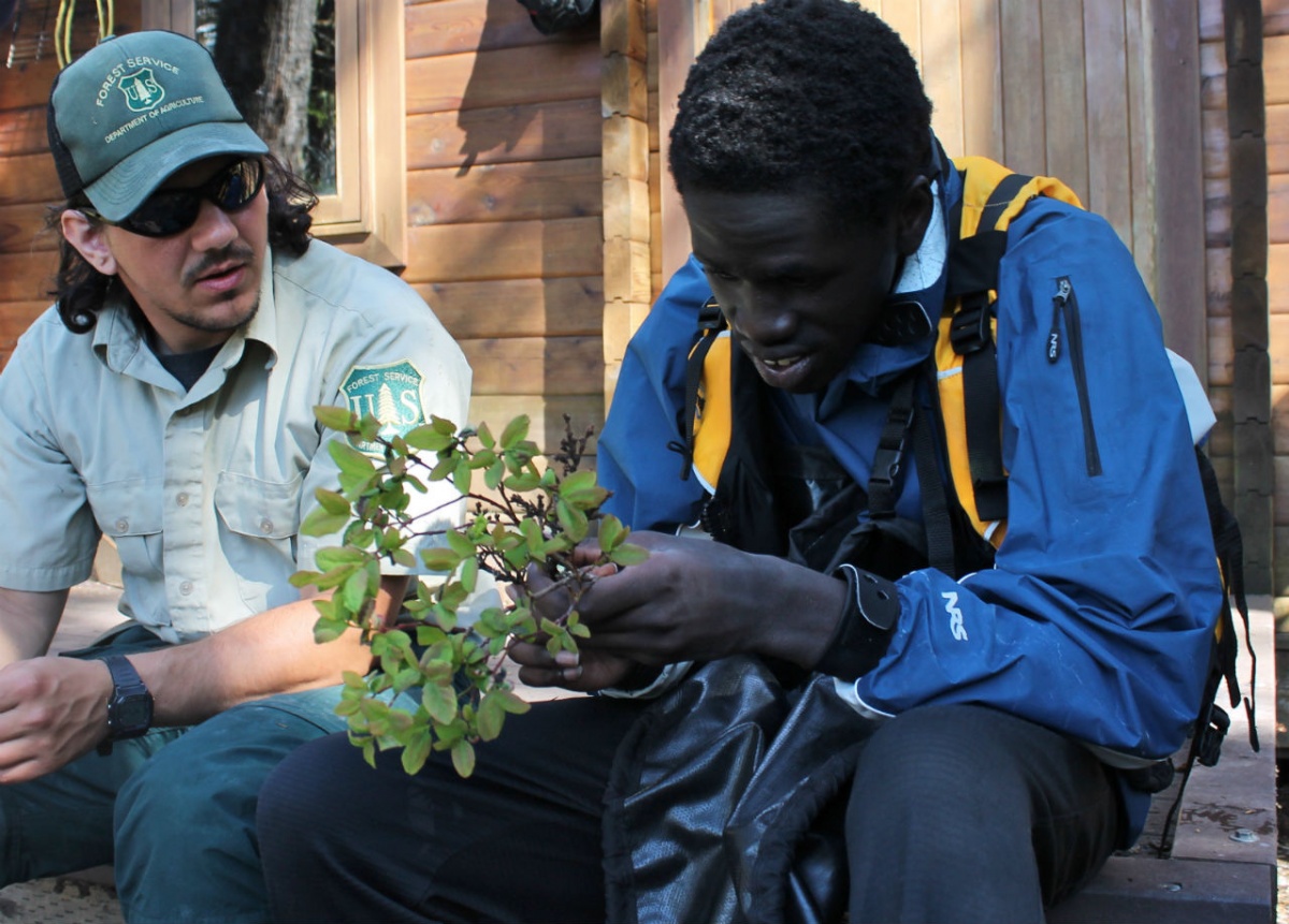 Reth sits on a porch with a Forest Service employee holding a plant sample.