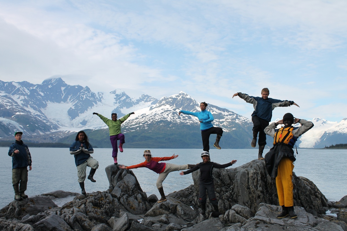 A group of young people pose on rocks in front of a lake in Alaska.