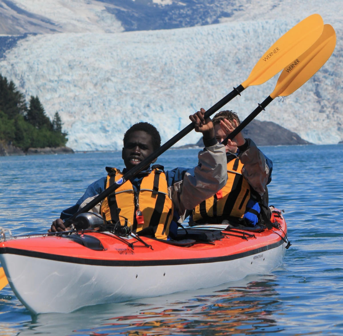 A young man paddles a kayak across  a lake in Alaska.
