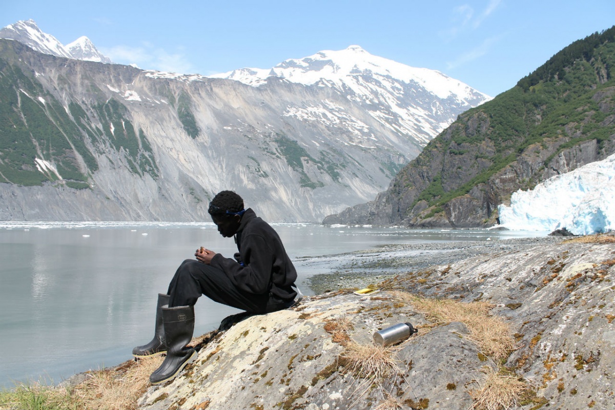 A young man sits on the bank of a lake in Alaska.