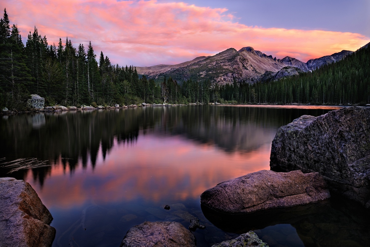 Un pico de montaña reflejado en un lago mientras el cielo se vuelve rosado