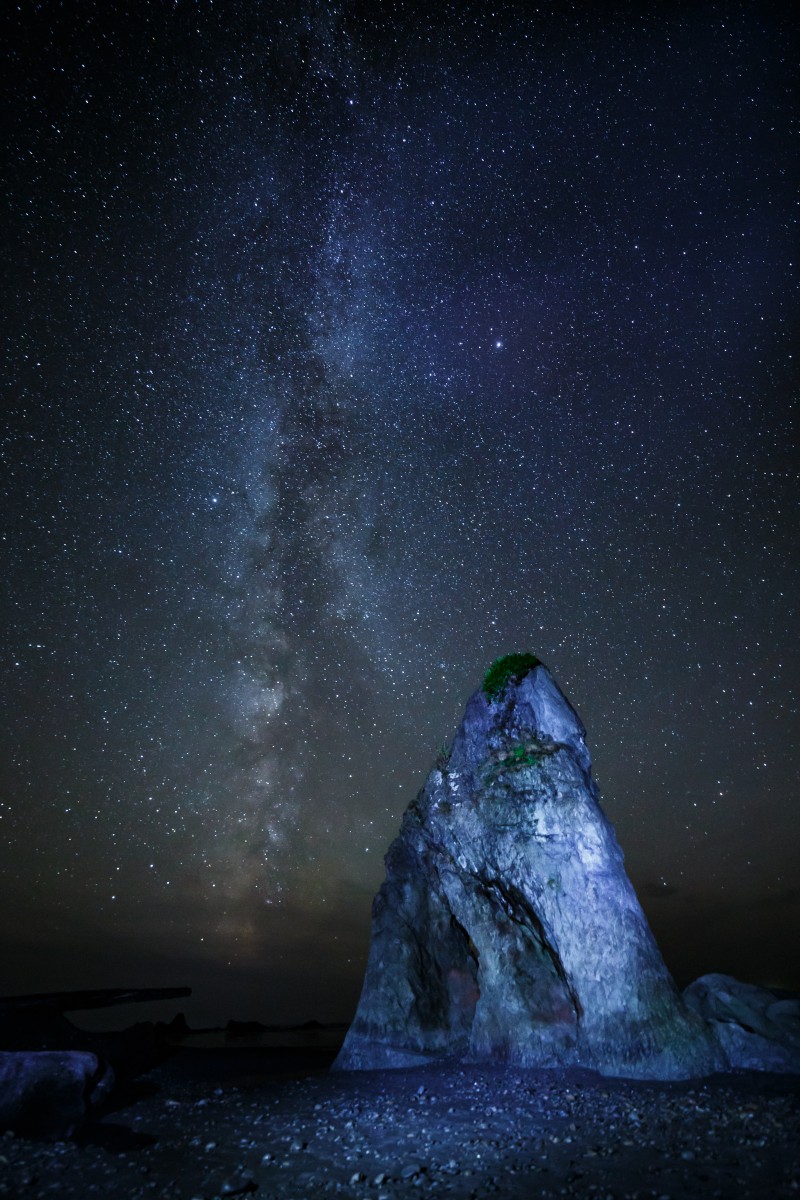 Night stars in sky over beach and large rock.
