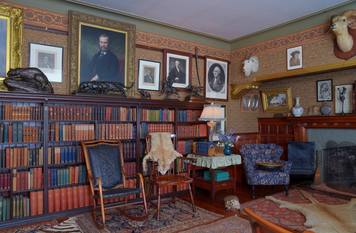 Picture of Theodore Roosevelt's library shows many bookshelves, paintings and mounted animals. 